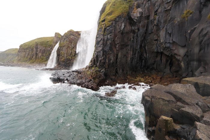 Two waterfalls plummet into the ocean in the misty Aleutians.