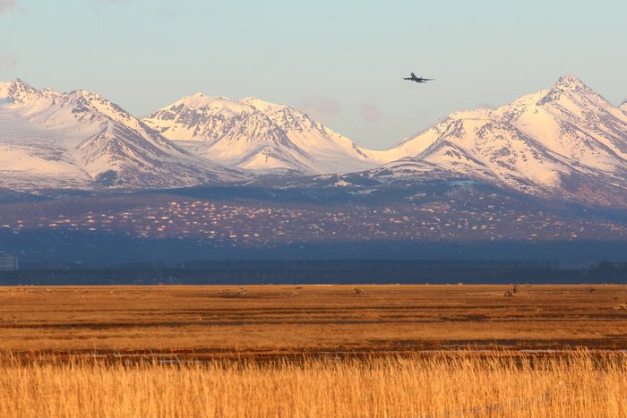 The Anchorage Hillside glows beneath the Chugach mountains and a passing jet. Viewed from across Knik Arm.