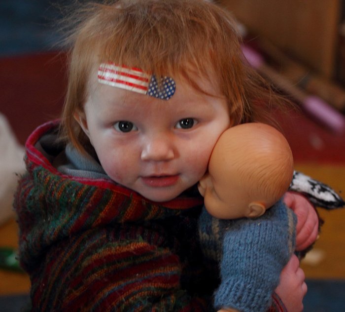 Lituya sporting a patriotic bandaid after a brief encounter with the woodstove, hugging her doll.