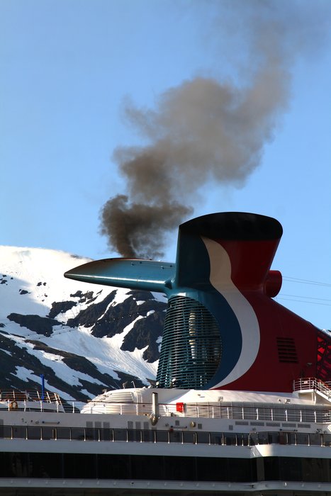 Smoke pours out of the smokestack of a cruise ship as it fires up its engines.