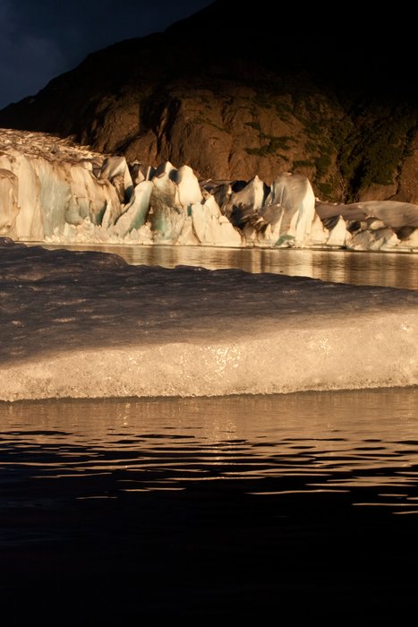 The snout of the glacier lit up with warm light.  Floating ice is seen in the foreground.