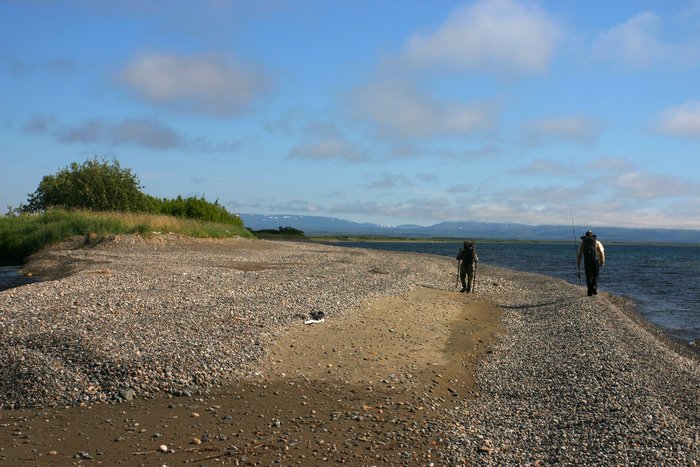 Walking on the gravel beach of Lake Iliamna, under a bright midday sun. 