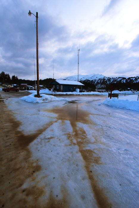As the street melts near the harbor in Seldovia, the resulting amber overflow paints a blue-ice parking lot.