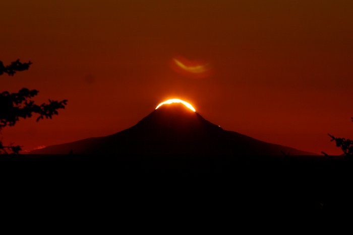 The sun is nearly eclipsed by the peak of Augustine Volcano.  The next day its arc through the sky was shifted enough it barely touched the peak.