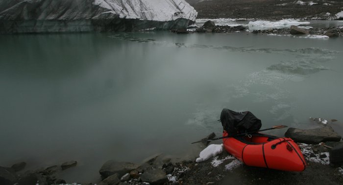 Packraft and remnant track through slush, dwarfed by glacial ice (close-up)
