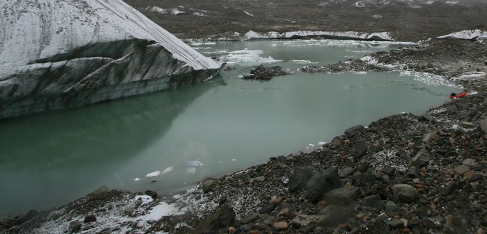 Packraft and remnant track through slush, dwarfed by glacial ice
