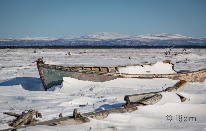 Along a frozen slough that cuts through the tundra lays a retired wooden skiff.