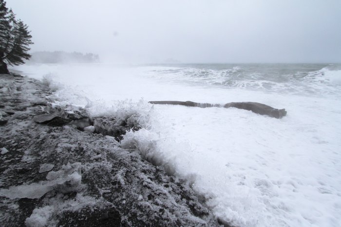 High tides and big waves wash gravel onto icy snow.