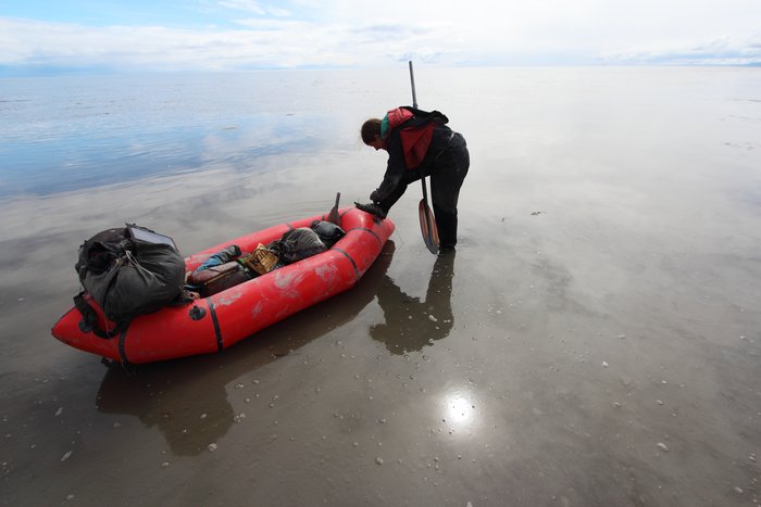 Erin ties a shoe on the glassy mudflats, covered with only an inch or two of water